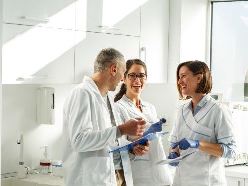 Three dentists laughing together and holding clipboards